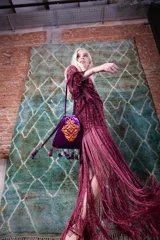 Cartera tipo saco de terciopelo de seda en color violeta, con diseño bordado en tono naranja en el frente. Presenta cierre mediante cordones ajustables con terminaciones de borlas y flecos decorativos en la base.