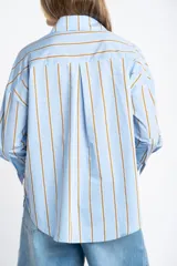 Camisa de algodón y poliamida, color celeste con rayas verticales en tono mostaza/marrón. Presenta un corte oversize, cuello clásico y mangas largas.