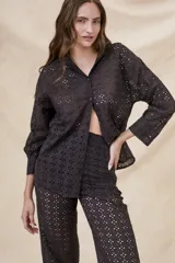 Camisa negra de algodón con bordado calado, corte oversize, cuello clásico, cierre frontal con botones y mangas largas con puños abotonados.