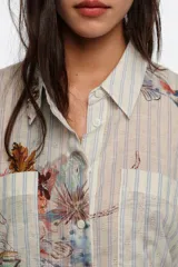 Camisa oversize de manga larga con patrón de rayas y estampado artístico multicolor, con cuello camisero, cierre frontal de botones y bolsillos en el pecho.