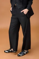 Pantalón sastrero de corte ancho y tiro alto, con diseño de líneas limpias, bolsillos laterales y cierre frontal con botón. Presenta una caída fluida y estructura amplia.