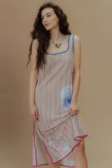 Vestido largo de tejido calado color beige, con estampado de flores en tonos rosados, celestes y verdes. Presenta escote cuadrado con ribete azul y terminaciones con crochet fucsia.