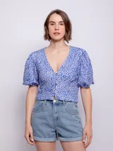 Top corto azul con estampado floral de flores blancas y naranjas. Presenta escote en V con cierre frontal de botones y mangas abullonadas cortas.