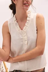 Top sin mangas color blanco con escote en V y volados en el cuello y la botonera delantera.