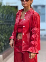 Camisa de cuero sintético color rojo, con cierre frontal de botones, cuello clásico y mangas largas con puños fruncidos y volados.