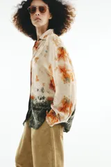 Camisa de manga larga con cuello solapa y cierre frontal con botones, con diseño tie-dye en tonos beige, naranja y verde oscuro en el sector inferior.