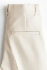 Pantalón tobillero cigarette de color beige en tejido elástico, con cintura estándar, bolsillos al bies y piernas ajustadas con raya marcada.