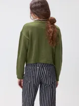 Cardigan de algodón grueso color rojo, con cuello redondo, cierre frontal de botones grandes y bolsillos cuadrados en el frente. Presenta detalles de pelo sintético en el cuello y los bolsillos, y logo bordado en uno de los bolsillos.