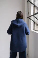 Tapado de paño azul con capucha, diseño de corte holgado y largo a la cadera. Presenta detalles en color negro en el interior, bordes y puños, con bolsillos frontales amplios y cierre frontal.