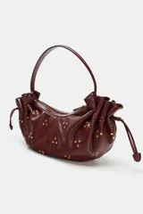 Bolso de hombro de diseño fruncido con cordones ajustables en los laterales y tachas metálicas doradas distribuidas por toda la superficie. Cuenta con asa corta de hombro y cierre superior con cremallera.