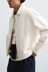 Cazadora de hombre, corte regular fit, color blanco roto, confeccionada en tejido de lino y algodón. Presenta cuello solapa, manga larga con puños abotonados, bolsillos de plastrón en la cadera y cierre frontal de botonadura.