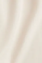 Pantalón de tejido liso color blanco roto o crema, de corte ancho y tiro alto con cintura elástica fruncida. Presenta pliegues frontales que le dan volumen a la pierna.