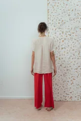 Blusa de lino color beige de calce relajado, con escote en V y detalles de pliegues frontales. Posee mangas cortas y una silueta suelta.