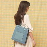 Cartera tipo tote de estructura vertical, color negro, con doble asa larga para llevar al hombro y correa desmontable y regulable. Cuenta con bolsillo frontal exterior de fácil acceso y detalles de costuras visibles.