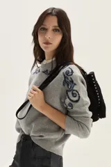 Sweater de tejido de punto color beige con diseño de arabescos en tonos marrones en hombros y mangas. Presenta cuello redondo con cordones decorativos y puños con textura acanalada.