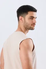 Musculosa beige jaspeado de corte clásico, con cuello redondo y diseño sin mangas. Presenta un pequeño estampado circular en el pecho con temática costera y la inscripción 'Paradise Bound'.