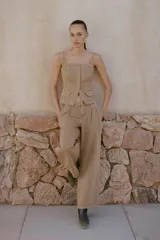 Top corto de denim color beige, con escote recto y tirantes finos ajustables. Presenta diseño con costuras verticales, cierre frontal con botones ocultos y dos bolsillos decorativos con solapa en la parte inferior.