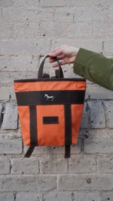 Mochila pequeña color borgoña con detalles en cuero marrón y aplique metálico de un caballo. Tiene manija superior y correas traseras regulables.