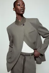 Blazer de corte estructurado en color verde oliva, con cuello subido en tejido a contraste de textura aterciopelada. Presenta cierre frontal con un solo botón, bolsillos con solapa en el delantero y un bolsillo superior tipo ojal.