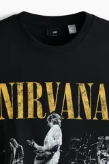 Remera de algodón color negro con cuello redondo y mangas cortas. Presenta un estampado frontal con el logo de la banda Nirvana en color amarillo y una imagen en blanco y negro del concierto Live at Reading.