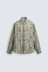 Camisa de corte relajado confeccionada en tejido fluido con estampado geométrico en tonos azules y ocres. Presenta cuello solapa, cierre frontal de botones y manga larga con puños abotonados.