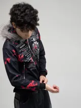 Campera con cierre frontal, confeccionada en poliéster con estampado gráfico tipo camuflado y tipografía. Presenta capucha con borde de piel sintética no removible y ajuste regular.