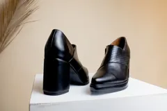 Botinetas negras de cuero con puntera fina, detalle de textura en el empeine, cierre lateral con cremallera y tacón cuadrado.