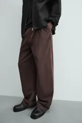 Pantalón jogger de algodón color marrón oscuro, de corte relajado y pierna ancha. Presenta cintura elástica con cordón ajustable y bolsillos laterales y uno trasero de plastrón.
