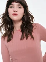 Remera de manga larga entallada en tejido pointelle, con escote bote y detalle de pequeño lazo central. Presenta un acabado con borde picot en el escote.