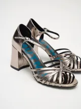 Sandalias de taco alto ancho con diseño retro, confeccionadas en charol negro. Presentan tiras delanteras múltiples entrelazadas, talón cerrado y una correa fina ajustable al tobillo con hebilla metálica.