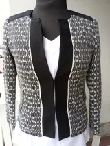 Chaqueta combinada en negro liso con tela estampada en blanco y negro, con vivos blancos, cierres en las mangas y bolsillos. Se prende con broches.