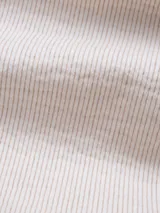 Camisa celeste a rayas verticales blancas, de manga larga con botones de madera y parche con logo de la marca en el ruedo.