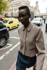 Blazer corto de corte estructurado con cuello solapa, manga larga y hombreras. Presenta cierre frontal con botones metálicos y dos bolsillos delanteros de plastrón con solapa. Diseño con estampado de cuadros tipo príncipe de gales.