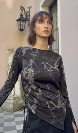 Top de manga larga color negro, confeccionado en jersey elástico. Presenta un diseño asimétrico con jaretas laterales regulables que permiten ajustar el largo y el volumen, y aberturas para los pulgares en los puños.
