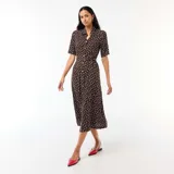 Vestido midi marrón con estampado de lunares blancos, estilo camisero con cuello solapa, mangas cortas, cierre frontal de botones y cinturón para anudar en la cintura.