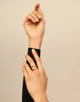 Anillo de metal bañado en plata con diseño curvilíneo de estilo oriental y logo de la marca grabado.