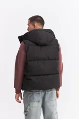 Chaleco puffer acolchado color azul marino, con capucha fija, cierre frontal con solapa de botones a presión y bolsillos laterales con cierre. Presenta un parche con el logo de la marca en el pecho.