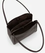 Cartera modelo hobo de gran tamaño, confeccionada en poliuretano con textura geométrica triangular. Presenta asas tubulares largas para llevar al hombro, cierre superior con cremallera y un pequeño aplique metálico dorado en la parte frontal.