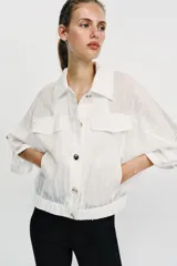 Blusa negra de cuello solapa y manga corta, con bolsillos con solapa en el pecho, bajo elástico y cierre frontal con botones.
