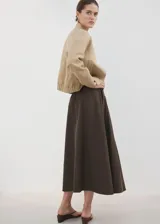 Falda midi evasé de tiro medio, color marrón oscuro, con diseño cruzado frontal y cierre de cremallera en la parte posterior, cuenta con forro interior.