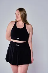 Conjunto deportivo compuesto por un top tipo bra de escote redondo y una pollera tableada corta, ambos en color negro con el logo 'bk.' estampado en blanco en la banda elástica.