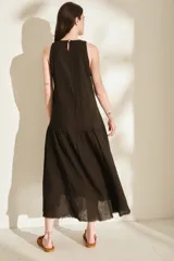 Vestido midi negro sin mangas, con cuello redondo, corte recto en la parte superior y falda amplia con vuelo. Presenta costuras decorativas verticales y un detalle deshilachado en el dobladillo inferior.