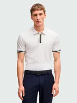 Remera polo blanca de corte regular fit, con cuello clásico y cierre de cremallera parcial. Presenta detalles de rayas en el cuello y en los puños de las mangas cortas.