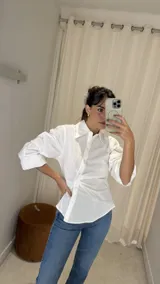 Camisa blanca de algodón con cuello clásico, mangas tres cuartos abullonadas y cierre frontal asimétrico con frunces laterales.