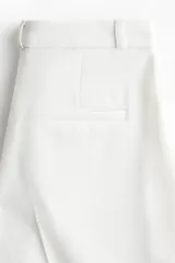Pantalón sastrero de color blanco, tiro alto, con cierre frontal de botón y piernas acampanadas con pliegues marcados.