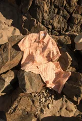 Camisa de lino de manga corta, con diseño oversize y estampado de rayas en color naranja y blanco. Presenta cuello camisero, cierre frontal de botones y un sutil bordado en la parte delantera.