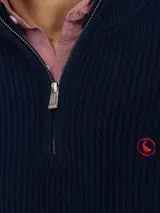 Sweater de punto acanalado en color azul marino, con cuello alto y cierre frontal parcial. Presenta mangas largas con puños acanalados y un pequeño logo bordado en rojo en el pecho.