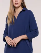 Vestido corto blanco de algodón, marca Dash, con cuello camisero, escote en V y bolsillos laterales. Presenta mangas tres cuartos y calce holgado con ruedo irregular.