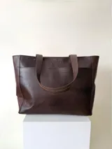 Cartera tipo shopper de cuero marrón texturado, con doble asa de hombro y un bolsillo frontal amplio con cierre de imán.
