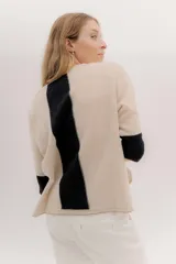 Buzo de punto en color negro con mangas tres cuartos y puños en contraste color marrón. Presenta un diseño holgado con tajos laterales y un aplique circular con logo en la parte inferior.